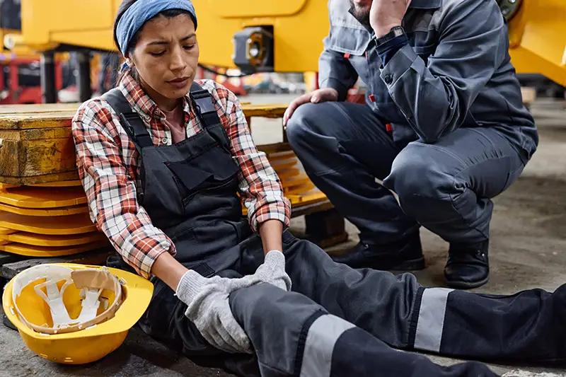 factory worker holding her knee in pain while coworker calls for help